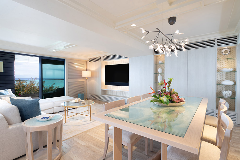 Dining area with table, chairs, and living area with TV, couch, balcony with ocean view.