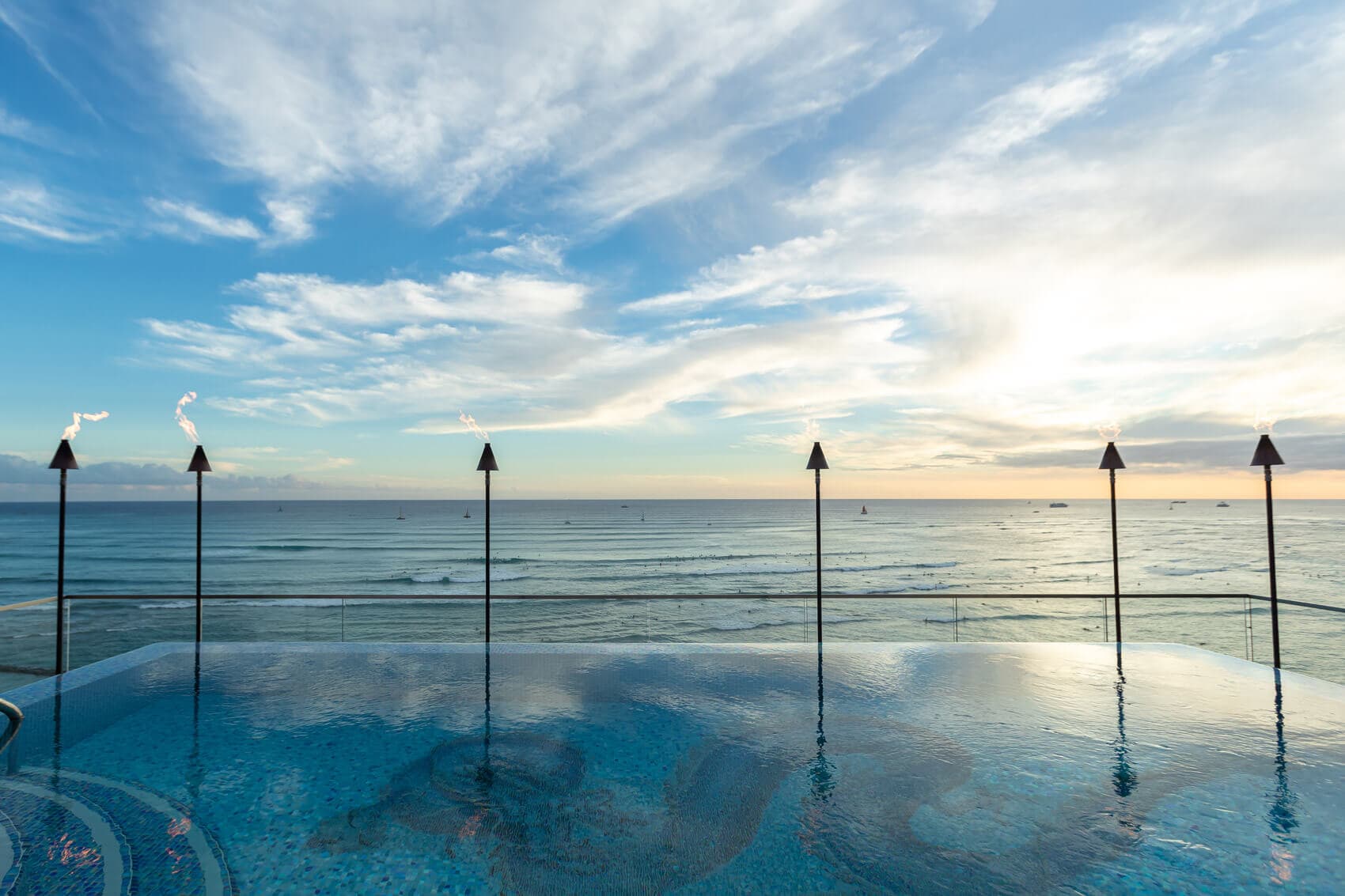 Torch lighting along edge of pool and ocean views.