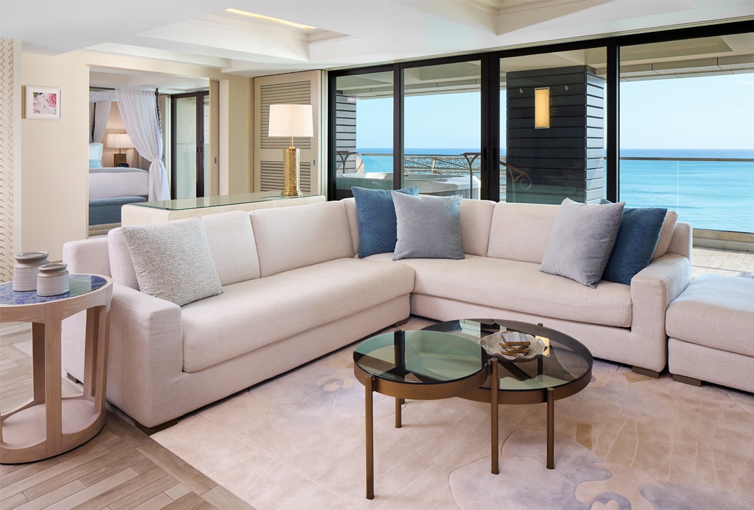 Living area with couch, table, lamps, and balcony with ocean views.