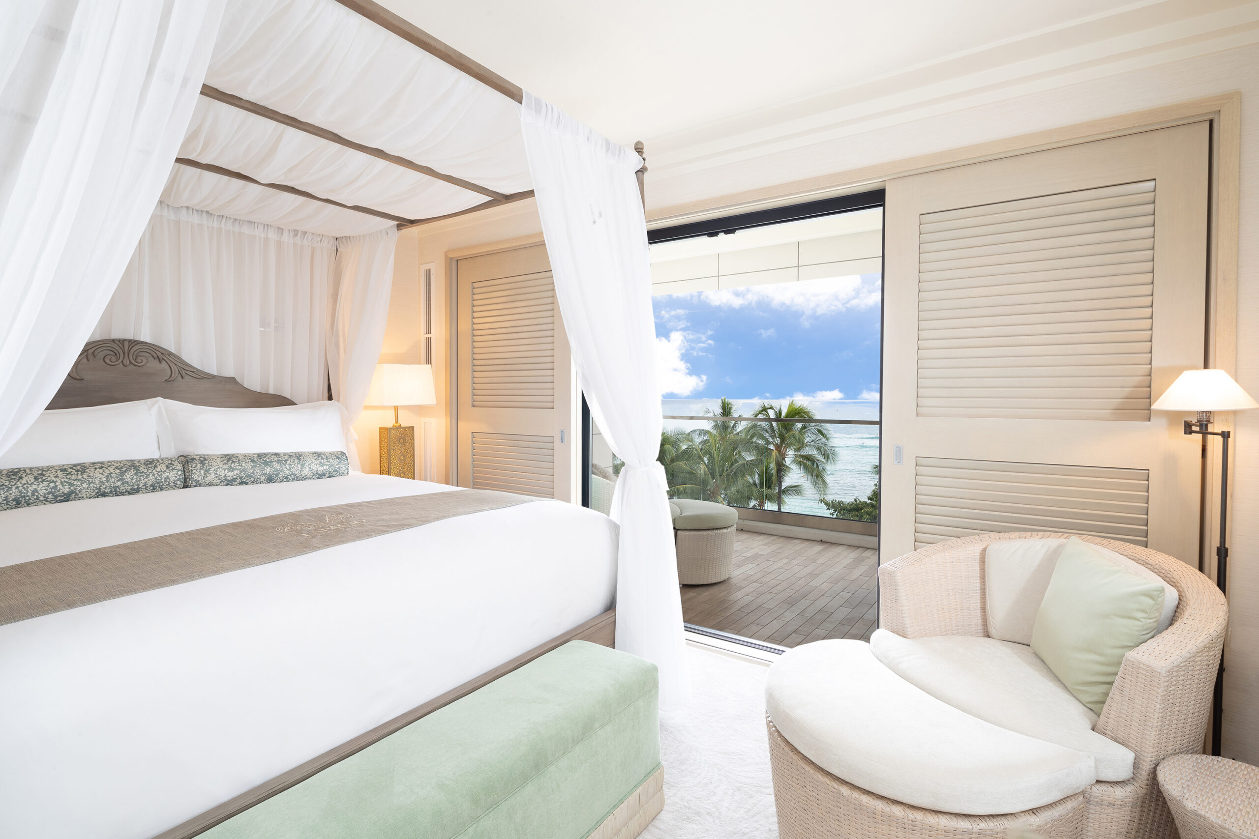 Room with canopy bed, lamps, seating, and balcony with ocean views.