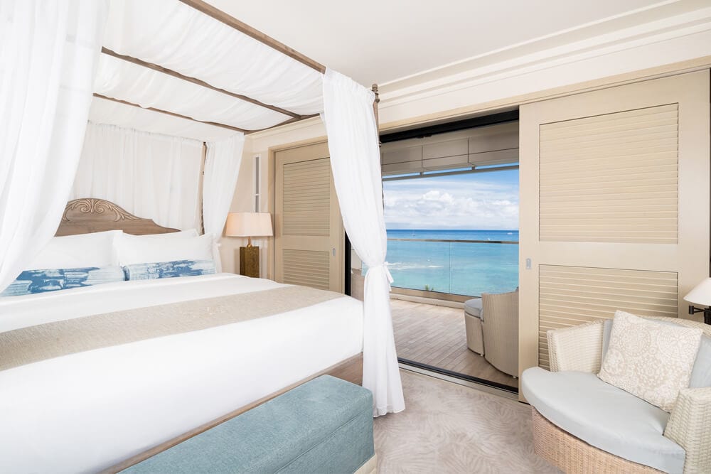 Room with canopy bed, lamps, and balcony with views of ocean.