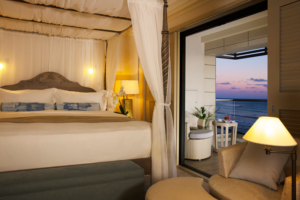 Room with canopy bed, lamps, night stands, and balcony with views of ocean.