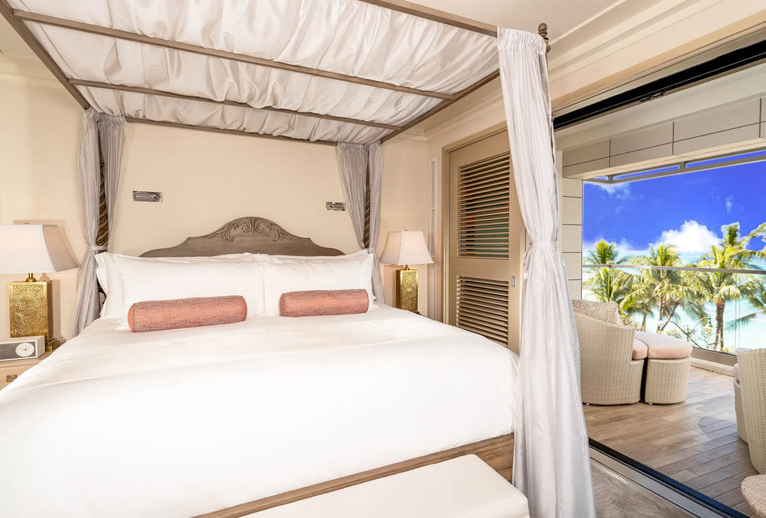 Room with canopy bed, lamps, nightstands, furnished balcony with ocean views.