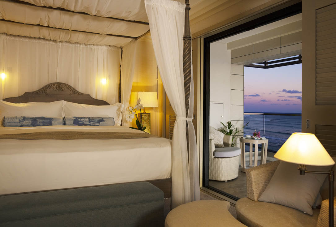 Room with canopy bed, lamps, furnished balcony with ocean view.